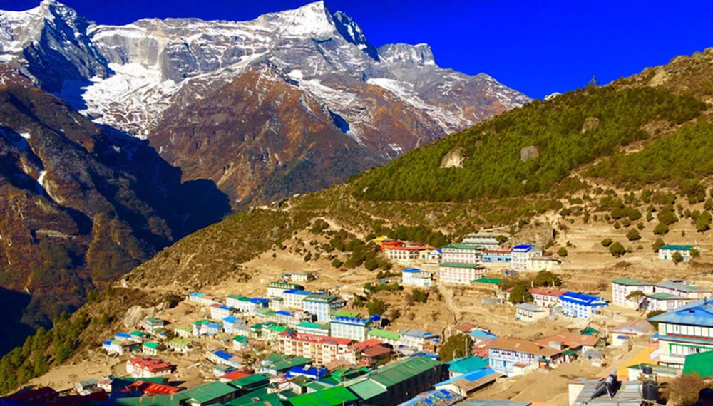 A high mountain village on a hillside beneath snow-covered rock peaks