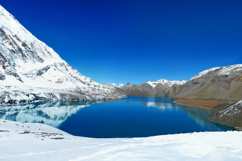 Snow-covered mountains reflected in a still turquoise glacial lake