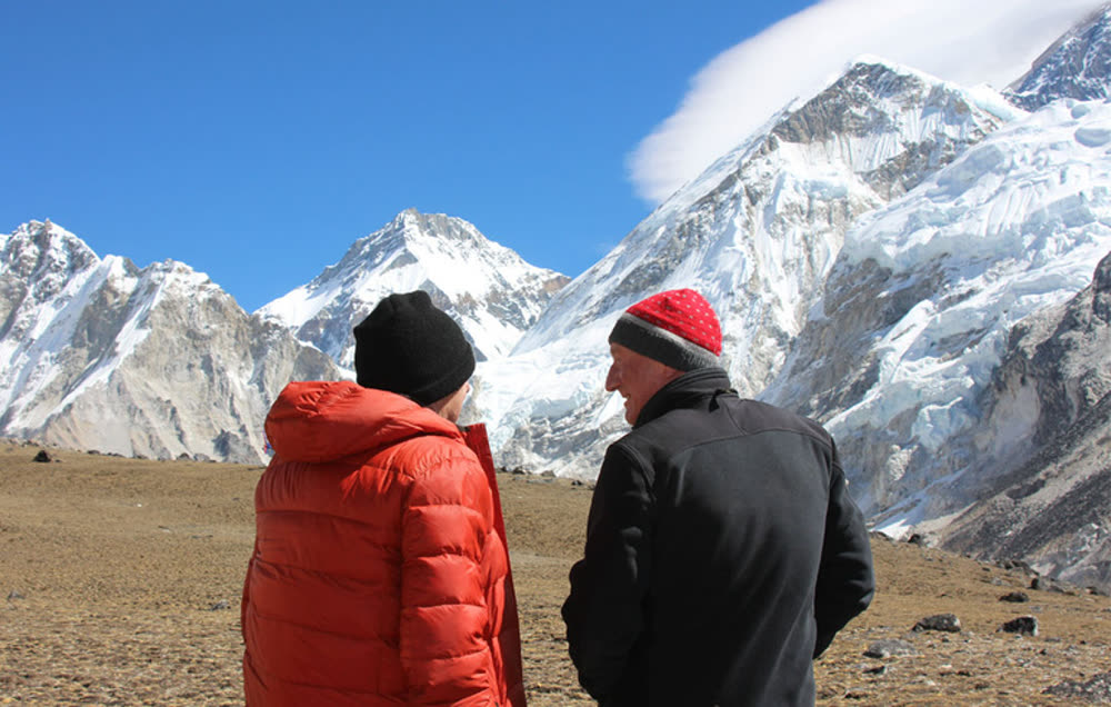 Climbers looking out at a wall of snow-covered Himalayan peaks under a clear sky