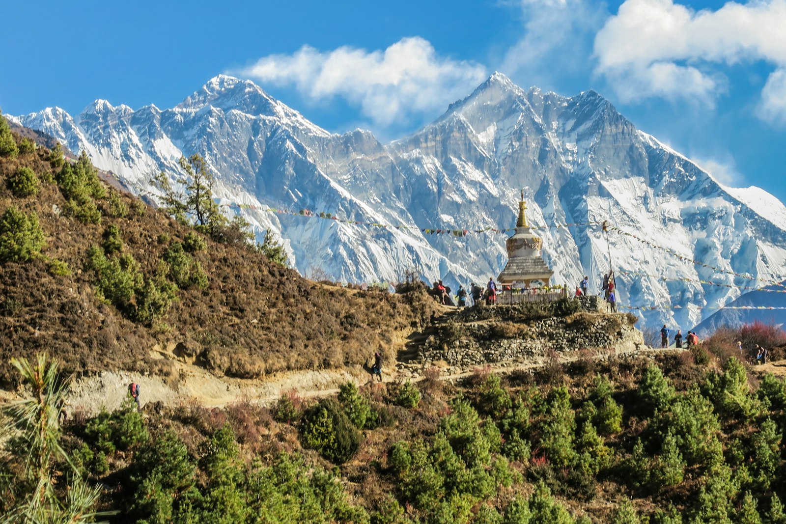 A stone stupa hung with prayer flags on a ridge below a vast wall of snow and ice