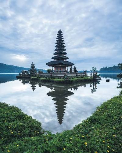 Balinese temple mirrored in still water beneath a blue sky