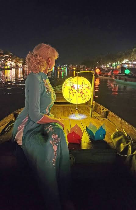 A woman in an ao dai on a lantern-lit boat at night in Hoi An